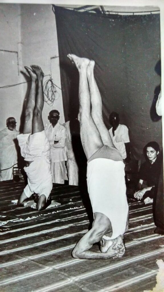 How to do the śiraśāsana (headstand pose) safely - Image 3: Yogacharya Sundaram demonstrating śiraśāsana at age 80+, looking on is his grand-daughter Sujata